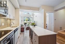 Modern kitchen featuring stainless steel appliances, light wood-finish flooring, white cabinetry, a large center island with seating, and glass tile backsplash - 