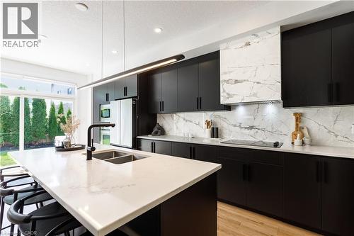 Modern kitchen featuring dark cabinetry, white countertops, and a full-height backsplash with a marble-like pattern - 916 Steepleridge Court, Kitchener, ON - Indoor Photo Showing Kitchen With Double Sink With Upgraded Kitchen