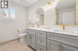 Bathroom featuring a dual vanity with light gray cabinetry, integrated white countertops, and gold-finish fixtures - 