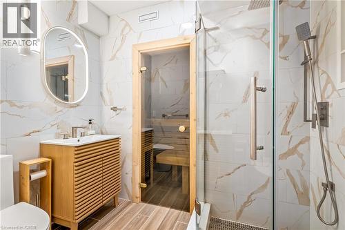 Modern bathroom featuring a glass-enclosed shower, a built-in sauna with wood paneling, a contemporary vanity with a slatted wood-finish cabinet, and a backlit oval mirror - 12 Buman Court, Barrie, ON - Indoor Photo Showing Bathroom