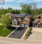 Brick and stone facade residence featuring a two-car garage, dark-toned roof, paved driveway, and manicured landscaping - 