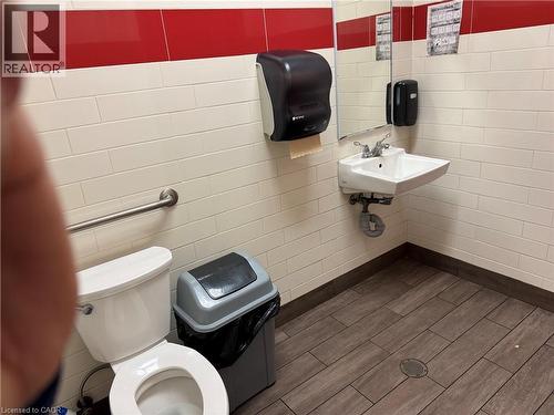 White tile walls with a red accent band, wood-finish flooring, wall-mounted sink, and a toilet with a grab bar - 255 King Street N, Waterloo, ON 