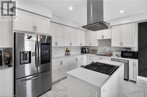 Kitchen featuring an island with a gas cooktop, white cabinetry, a stainless steel refrigerator, white quartz countertops, and a mosaic tile backsplash - 9 Fleming Crescent, Caledonia, ON - Indoor Photo Showing Kitchen