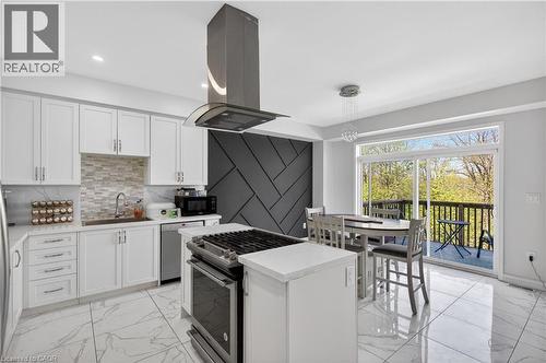 Contemporary kitchen featuring white cabinetry, a stone-finish backsplash, and a central island with a gas range - 9 Fleming Crescent, Caledonia, ON - Indoor Photo Showing Kitchen