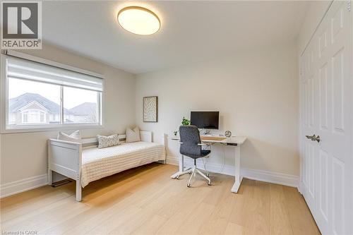 This room features light-colored hardwood flooring, a large window providing ample natural light, and a white paneled door - 4267 Sarazen Drive, Burlington, ON - Indoor Photo Showing Bedroom
