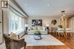 Open-concept living area featuring rich wood flooring throughout, a wide bay window with integrated seating, recessed ceiling lighting, and a dining area illuminated by a multi-bulb pendant fixture - 