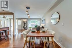 Expansive dining area featuring wood-finish flooring, a contemporary chandelier, a large window, a round wall mirror, and neutral wall tones - 