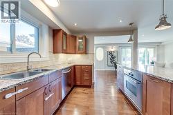 Kitchen featuring wood-finish flooring, undermount dual-basin sink, granite countertops, and stainless steel appliances - 