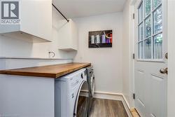 Laundry area featuring a wood-finish countertop, integrated appliances, white cabinetry, and wood-finish flooring - 