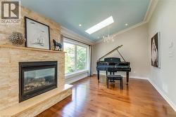 Living area featuring a stone-clad fireplace with a hearth, expansive windows, wood-finish flooring, a vaulted ceiling with a skylight, and a decorative chandelier - 