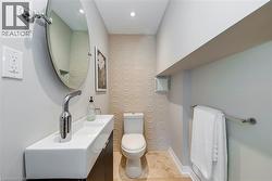 Powder room featuring a wall-mounted rectangular sink with a chrome faucet, a circular mirror, and textured wall tiling - 