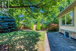 Expansive backyard featuring a lush lawn, mature trees, and a patterned stone patio - 