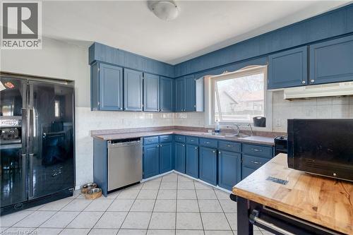 Kitchen featuring blue cabinetry, a stainless steel dishwasher, a black side-by-side refrigerator, white tile flooring, and a window above the sink - 151 Winchester Boulevard, Hamilton, ON - Indoor Photo Showing Kitchen