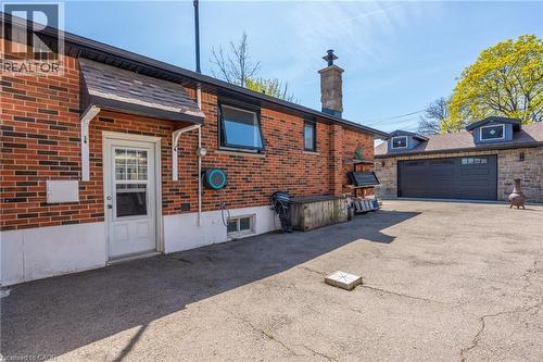 Brick exterior with white door, stone chimney, and an attached two-car garage featuring a dark sectional door and two dormer windows - 151 Winchester Boulevard, Hamilton, ON - Outdoor