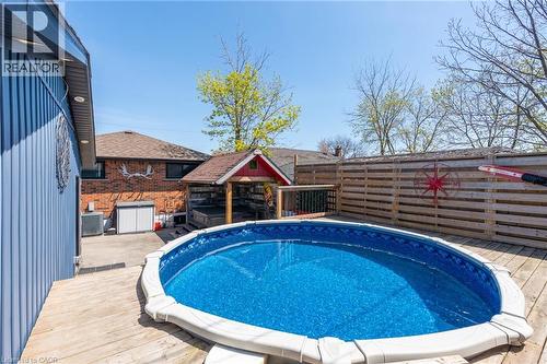 Backyard featuring an above-ground pool with surrounding wood decking, a covered hot tub area, and a horizontal wood privacy fence - 151 Winchester Boulevard, Hamilton, ON - Outdoor With Above Ground Pool