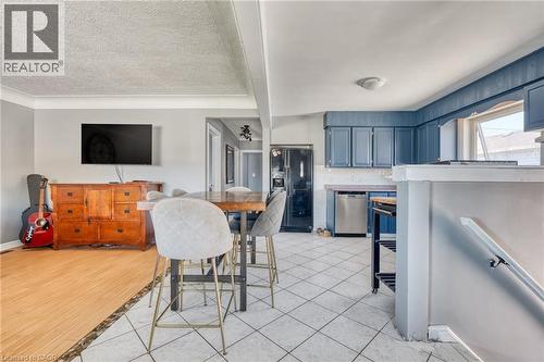 Kitchen and living area featuring a wood-finish flooring, tiled kitchen flooring, blue cabinetry, stainless steel dishwasher, and a window above the sink - 151 Winchester Boulevard, Hamilton, ON - Indoor Photo Showing Other Room