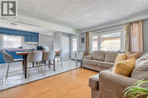 Open-concept living space featuring hardwood-style flooring, a large picture window, and a kitchen with blue cabinetry, white tile backsplash, and an island with seating - 151 Winchester Boulevard, Hamilton, ON - Indoor Photo Showing Living Room