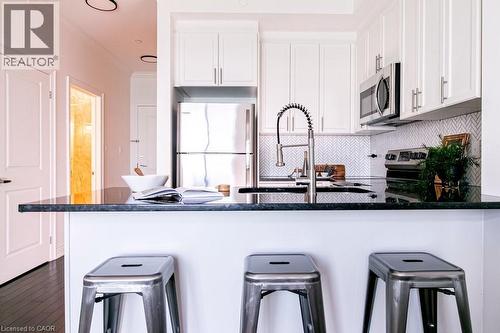 Kitchen featuring stainless steel appliances, dark countertops, white shaker cabinetry, a herringbone tile backsplash, and dark wood-finish flooring - 101 Shoreview Place Unit# 631, Stoney Creek, ON - Indoor Photo Showing Kitchen