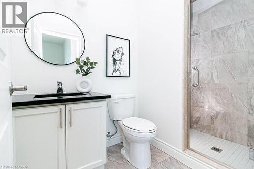 Bathroom featuring a glass-enclosed shower with large-format stone-look tile, white vanity with dual doors and brushed nickel hardware, black countertop, and a circular mirror - 101 Shoreview Place Unit# 631, Stoney Creek, ON - Indoor Photo Showing Bathroom