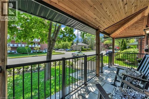 Covered front porch featuring a natural wood-finish ceiling, dark metal railings, square paver flooring, and exposed wood support posts - 25 Park Street E, Hamilton, ON - Outdoor With Deck Patio Veranda With Exterior