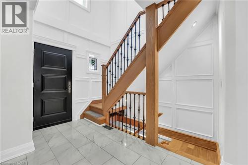 Foyer featuring a black paneled entry door, light wood staircase with wrought iron balusters, white wainscoting, and large format tile flooring - 25 Park Street E, Hamilton, ON - Indoor Photo Showing Other Room