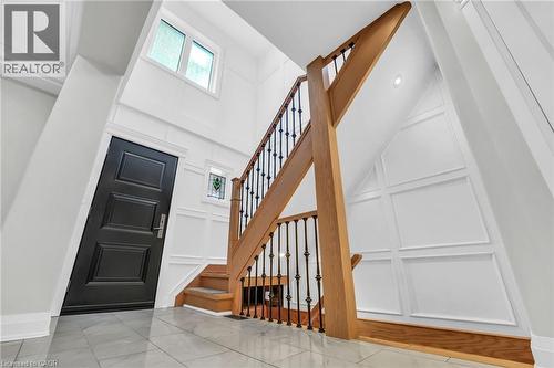 Two-story foyer featuring a wood staircase with wrought iron balusters, white wainscoting paneling, and a black paneled entry door - 25 Park Street E, Hamilton, ON - Indoor Photo Showing Other Room