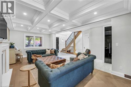 Open concept living space featuring a coffered ceiling with recessed lighting, herringbone wood-finish flooring, a white mantel, and a prominent staircase with dark iron balusters - 25 Park Street E, Hamilton, ON - Indoor