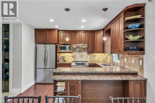 Kitchen featuring wood cabinetry, stainless steel appliances, speckled countertops, a tiled backsplash, and wood-finish flooring - 25 Park Street E, Hamilton, ON - Indoor Photo Showing Kitchen With Double Sink