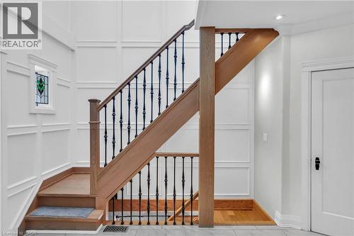 Hardwood staircase featuring wrought iron balusters, a natural wood-finish handrail, and a stained glass window accent - 25 Park Street E, Hamilton, ON - Indoor Photo Showing Other Room