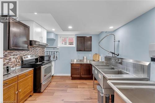 Kitchen area featuring stainless steel commercial-style sinks with a pre-rinse faucet, wood-finish flooring, recessed lighting, and a mosaic tile backsplash - 139 Ferris Drive, Wellesley, ON - Indoor Photo Showing Kitchen With Stainless Steel Kitchen With Double Sink With Upgraded Kitchen