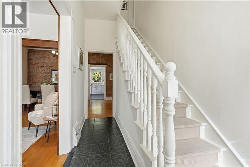 Foyer featuring white painted staircase with carpet runner, dark tiled flooring, and exposed brick wall accents - 314 Hess Street S, Hamilton, ON - Indoor Photo Showing Other Room