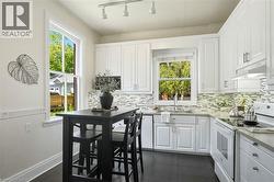 Kitchen featuring white shaker-style cabinetry, a mosaic tile backsplash, stainless steel sink, and gray countertops - 