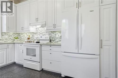 Bright kitchen featuring white shaker cabinetry, a mosaic tile backsplash, stone-finish countertops, stainless hardware, and black tile flooring - 314 Hess Street S, Hamilton, ON - Indoor Photo Showing Kitchen