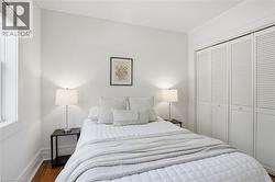 Bedroom featuring wood-finish flooring, a window with blinds, and white louvered bifold closet doors - 