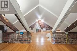 Attic space featuring pitched white ceilings, exposed brick walls, light wood-finish flooring, and structural wood beams - 