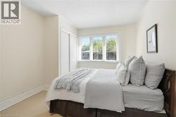 Bedroom featuring a window with horizontal blinds, light-colored carpeting, white baseboards, and a built-in closet with sliding doors - 