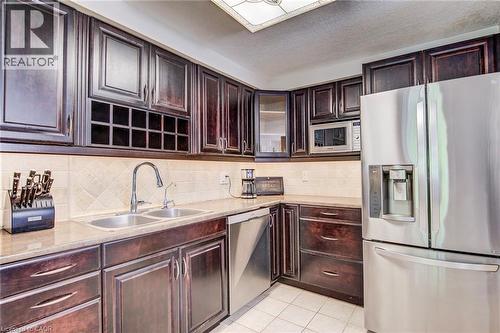 Kitchen featuring dark wood cabinetry, stainless steel appliances, light-toned countertops, a tile backsplash, and a double basin sink with a gooseneck faucet - 702 Elgin Street N, Cambridge, ON - Indoor Photo Showing Kitchen With Double Sink