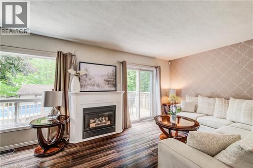 Living area featuring a white mantel fireplace, wood-finish flooring, patterned accent wall, and a sliding glass door opening to an outdoor deck - 702 Elgin Street N, Cambridge, ON - Indoor Photo Showing Living Room With Fireplace