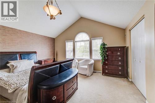Vaulted ceiling room featuring a decorative pendant light, textured accent wall, arched window, two additional windows with blinds, and light-colored carpeting - 702 Elgin Street N, Cambridge, ON - Indoor Photo Showing Bedroom