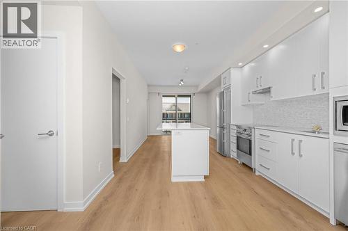 Modern kitchen featuring white cabinetry, stainless steel appliances, a white island with an extended countertop, a textured white backsplash, and wood-finish flooring - 10 Esplanade Lane Unit# 310, Grimsby, ON - Indoor Photo Showing Kitchen With Upgraded Kitchen