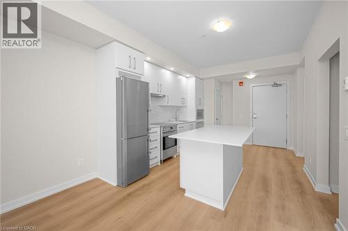 Contemporary kitchen featuring a central island with a white countertop, stainless steel appliances, white cabinetry, and wood-finish flooring - 10 Esplanade Lane Unit# 310, Grimsby, ON - Indoor Photo Showing Kitchen