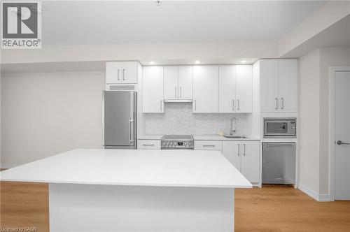 Modern kitchen featuring a white center island, stainless steel appliances, white cabinetry, and wood-finish flooring - 10 Esplanade Lane Unit# 310, Grimsby, ON - Indoor Photo Showing Kitchen