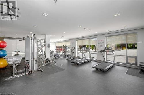 Spacious fitness room featuring rubber flooring, multiple cardio machines, strength training equipment, and large windows with roller shades - 10 Esplanade Lane Unit# 310, Grimsby, ON - Indoor Photo Showing Gym Room