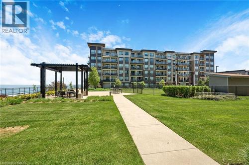 Manicured green space featuring a concrete pathway, a modern pergola with outdoor seating, and a multi-story building with balconies - 10 Esplanade Lane Unit# 310, Grimsby, ON - Outdoor With Facade