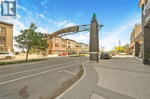 Urban streetscape featuring a brick monument with an overhead sign, paved sidewalks, and a tree-lined street - 10 Esplanade Lane Unit# 310, Grimsby, ON - Outdoor