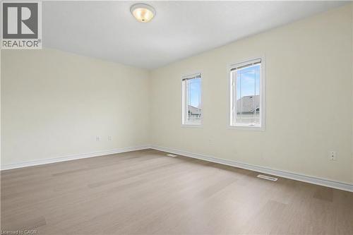 Spacious room featuring light-toned walls, wood-finish flooring, two large windows, a ceiling-mounted light fixture, and white baseboards - 619 Wild Ginger Avenue Unit# C15, Waterloo, ON - Indoor Photo Showing Other Room