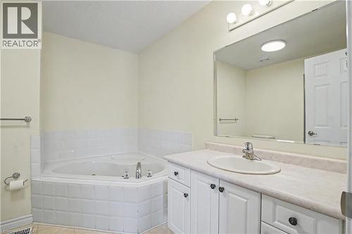 Bathroom featuring a corner built-in tub, vanity with integrated sink, spacious mirror, and overhead lighting - 619 Wild Ginger Avenue Unit# C16, Waterloo, ON - Indoor Photo Showing Bathroom
