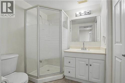Contemporary bathroom featuring a corner shower with frosted glass enclosure, a white vanity with paneling, a countertop with integrated sink, a rectangular mirror, and overhead vanity lighting - 619 Wild Ginger Avenue Unit# C16, Waterloo, ON - Indoor Photo Showing Bathroom