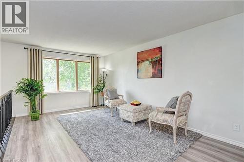 Wood-finish flooring throughout, featuring a large multi-pane window with neutral drapes, white walls, and a black metal railing - 92 Pinemeadow Crescent, Waterloo, ON - Indoor