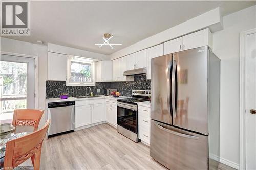 Kitchen featuring white cabinetry, stainless steel appliances, a dark mosaic tile backsplash, and light wood-finish flooring - 92 Pinemeadow Crescent, Waterloo, ON - Indoor Photo Showing Kitchen